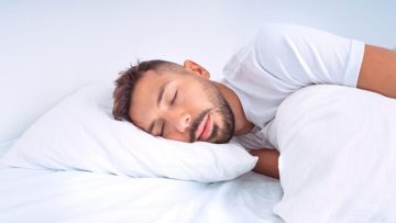 Handsome cute man sleeping in the bed with white beddings. Man lying on the pillow and enjoying good healthy sleep